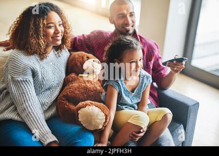 Die Elternschaft wählt familienfreundliche Filme für einen Sonntagnachmittag. Eine glückliche junge Familie von drei Kindern schaut zu Hause vom Sofa aus fern. Stockfoto