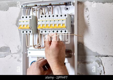 Elektroarbeiten, Kundendienst, Elektroingenieur verbindet Drähte mit den Klemmen in Schaltanlagenleistungsschaltern. Stockfoto