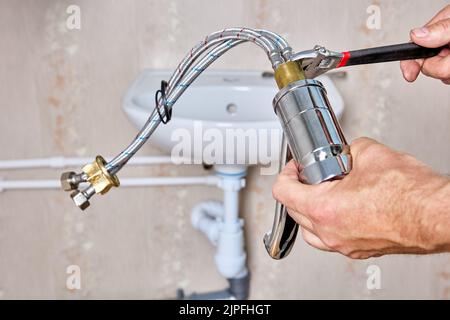 Klempner fixiert Verbindungsschläuche auf Wasserhahn, bevor Wasserhahn auf Waschbecken im Bad installiert wird. Stockfoto