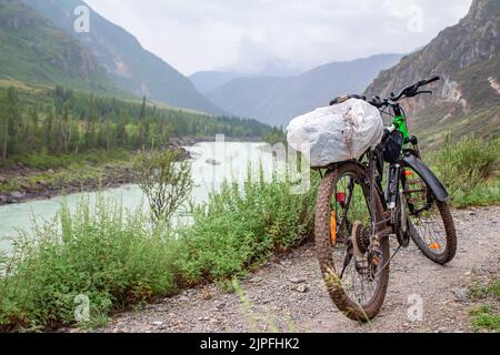 Blick auf ein schmutziges Sport-Mountainbike, das auf einem Steinpfad steht, ein Weg vor dem Hintergrund eines Flusses in einem hochgelegenen Tal Stockfoto