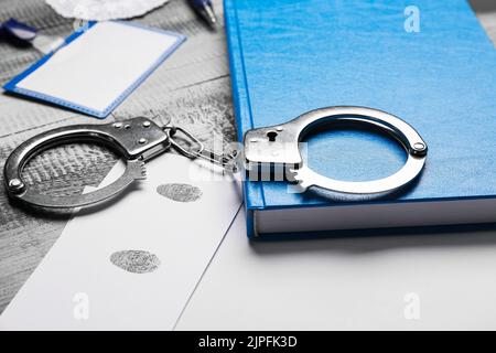 Papierbogen mit Fingerabdrücken, Handschellen und Notizbuch auf dem Tisch Stockfoto