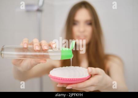 Eine entkokende Frau steht in der Badkabine und quetscht erfrischendes Duschgel auf einem Waschlappen im Badezimmer. Hautpflege und Körperpflege Badekonzept. Selektiv Stockfoto