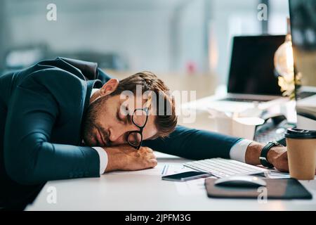 Er ist ein hart arbeibender Kerl. Ein müder junger Geschäftsmann schläft tagsüber auf seinem Schreibtisch im Büro. Stockfoto