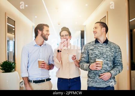 Es ist Zeit für eine Kaffeepause. Porträt einer Gruppe junger Geschäftsleute, die beim Kaffeetrinken gemeinsam einen Gang entlang gehen. Stockfoto