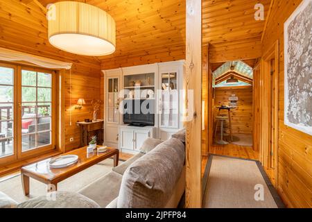 Gemütliches Interieur eines Landhauses aus Holz. Geräumiges Wohnzimmer und Blick auf eine kleine Küche mit Barstühlen Stockfoto