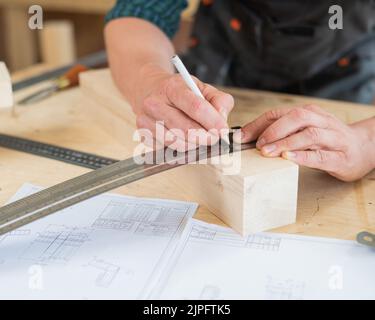 Ein Zimmermann mißt Holzbohlen und macht in einer Werkstatt mit einem Bleistift Markierungen. Stockfoto