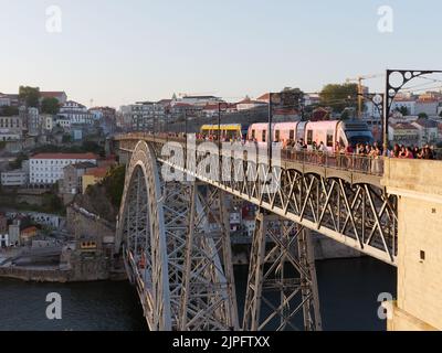 Ribeira-Viertel in Porto auf der anderen Seite des Douro-Flusses, während die Menschen die Aussicht von der Luis-I-Brücke bewundern und eine U-Bahn die Brücke, Portugal, überquert. Stockfoto