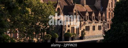 BRÜGGE, BELGIEN - 11. AUGUST 2022: Panorama mittelalterlicher Gebäude entlang eines Kanals bei Abendsonne Stockfoto