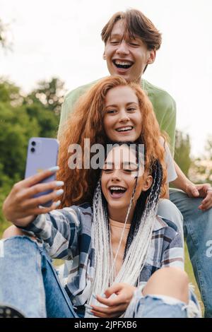 Drei moderne Freunde spielen im Sommerpark in der Social Media App Musik-Aufnahmen-Vlog. Glückliche Kinder können zu Hause spielen und Hobby lernen. Stockfoto