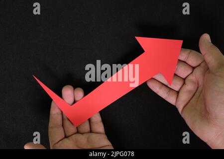 Menschliche Hände halten roten Pfeil nach oben in dunkelschwarzem Hintergrund. Wirtschaft und Wirtschaft erholen sich von Krise und Inflation Konzept. Stockfoto