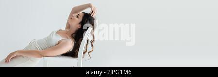 Seitenansicht eines langhaarigen Modells, das neben einem Stuhl auf einem grauen Banner posiert Stockfoto