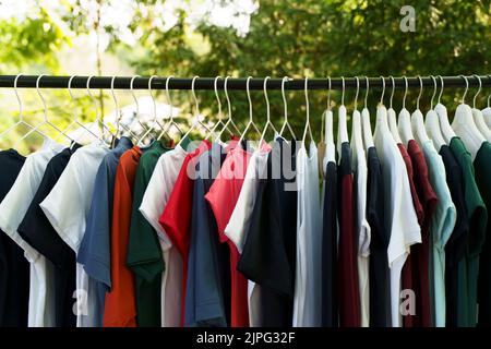 Farbige Kleidung, T-Shirts, auf Kleiderbügeln auf dem Markt. Hochwertige Fotos Stockfoto