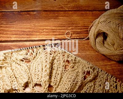 Prozess des Strickens. Stricknadeln, Schlaufen auf Stricknadeln, Strickstoff, Fadenknäuel, grobes Baumwoll- und Leinengarn, Holzhintergrund Stockfoto