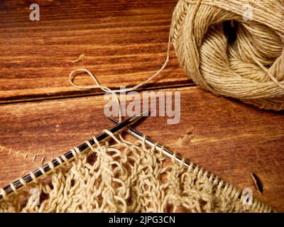 Durchbrochene Tischdecke beim Stricken. Stricknadeln, Schlaufen auf Stricknadeln, Strickstoff, Fadenknäuel, grobe Baumwolle und Leinen Stockfoto