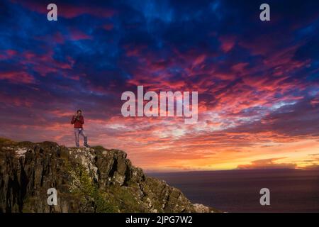 Eine wunderschöne Aufnahme eines Mannes, der auf einem Berg unter den bunten Wolken in Dumfries, Großbritannien, steht Stockfoto