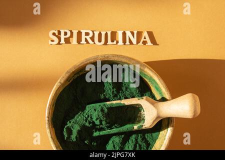Blau-grüne Algen Spirulina Pulver in Bambus Öko-Schale mit Text SPIRULINA, Nahrungsergänzungsmittel für vegane, vegetarische oder pflanzenbasierte Ernährung Multivitamine B12, Super Pulver in Löffel. Nahrungsergänzung Quelle von Protein und Beta-Carotin Stockfoto
