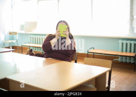 Die Lehrerin versteckt ihr Gesicht hinter dem Buch. Lehrer am Tisch. Lustiges Bild des Lehrers. Lehrer in Russland. Stockfoto