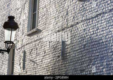 Straßenlampe auf dem Hintergrund einer weiß gestrichenen Ziegelmauer unter einem aufrackenden Licht. Stockfoto