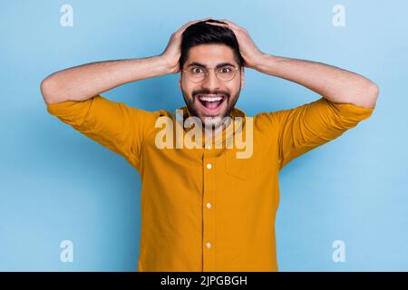 Foto von sprachlos starren verrückten Mann tragen gelbe Hemd halten Hände auf dem Kopf unglaublich unerwarteten Verkauf auf blauem Hintergrund isoliert Stockfoto