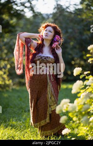 Porträt einer schönen, reifen Frau mit roten Haaren, die in einem Nymphen-Kleid gekleidet ist, das von Künstlern des frühen 20.. Jahrhunderts inspiriert wurde. Stockfoto