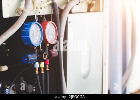 Luftreparaturmechaniker mit Messgeräten zum Befüllen von industriellen Klimaanlagen und zur Überprüfung der Wartung der Außenluftkompressoreinheit. Stockfoto