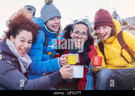 Multikulturelle Gruppe von Wanderern, die auf dem Berg sitzen und Kaffee mit Rucksäcken trinken Stockfoto