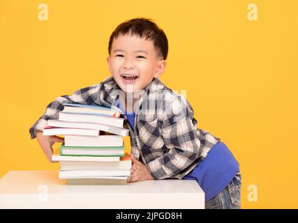 Glücklicher kleiner Junge, der große Bücher auf gelbem Hintergrund hält Stockfoto