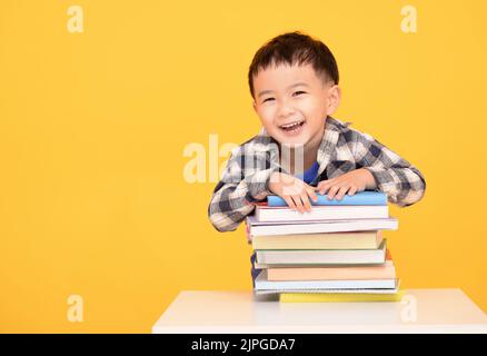 Glücklicher kleiner Junge, der große Bücher auf gelbem Hintergrund hält Stockfoto