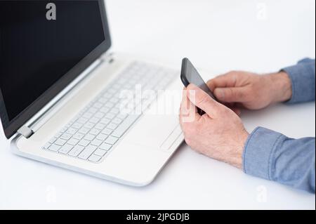 Mann hat das Telefon und den Computer-Laptop in die Hand. Online-Arbeit am Bürotisch. Laptop mit Platz für Text. Trend-Trading-Konzept für Kryptowährungen. Stockfoto