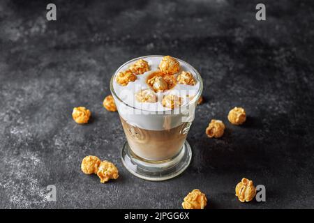 Kaffee-Latte in einer Glastasse mit Karamell-Popcorn auf grauem Beton Stockfoto