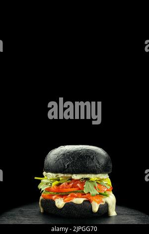 Schwarzer Burger mit Lachs, Gemüse und Käse auf schwarzem Hintergrund Stockfoto