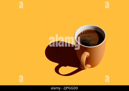 Braune Tasse voller Kaffee mit hartem Schatten auf gelbem Hintergrund mit Platz zum Kopieren Stockfoto