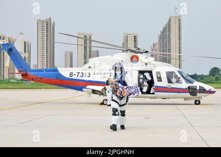 YANTAI, CHINA - 18. AUGUST 2022 - ein Mitglied der Luftbesatzung des Rettungsflugteams trägt ein krankes Kind beim Aussteigen aus einem Hubschrauber auf dem Penglaishaheko Stockfoto