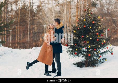 Junge Erwachsene Paar schmückt weihnachtsbaum im Winterwald. Neues Jahr Kiefer Urlaub Party-Konzept Stockfoto