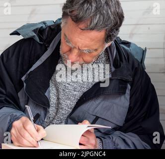 Ein Mann mit Bart und grauen Haaren schreibt ein Buch Stockfoto