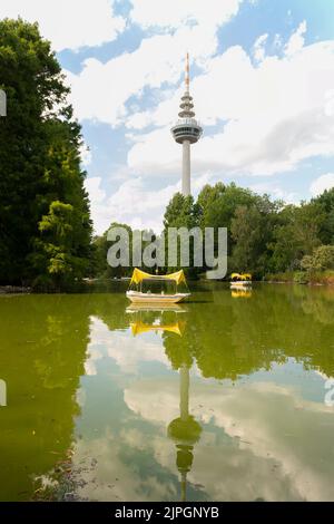 Der Telekommunikationsturm im Luisenpark in Mannheim, Deutschland, mit einem Teich und sattgrünen Bäumen im Hintergrund Stockfoto