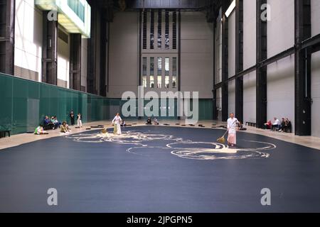 Künstler in traditioneller Kleidung schieben Reis mit Besen in einer Arbeit mit dem Titel „labyrinthisch“ des Künstlers Lee Mingwei. In der Haupthalle des Kraftwerks b Stockfoto