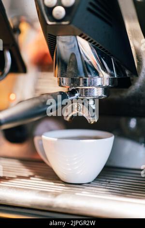 Eine professionelle Espresso-Kaffeemaschine aus Edelstahl mit einer frisch zubereiteten Tasse Espresso Stockfoto