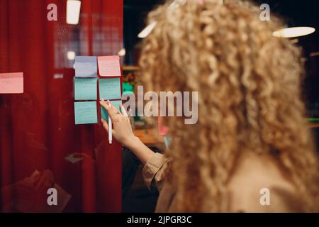 Geschäftsleuten Frau schreiben auf Haftnotiz auf Glaswand mit Kollegen stehen im Büro. Planung und Analyse der Teamarbeit Stockfoto