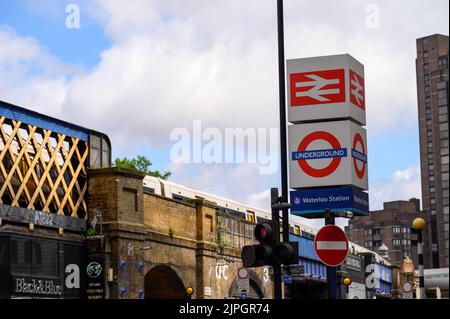 LONDON - 20. Mai 2022: Bahnhofschilder und U-Bahnhofschilder vor der Waterloo Station. Zug auf Brücke im Hintergrund Stockfoto