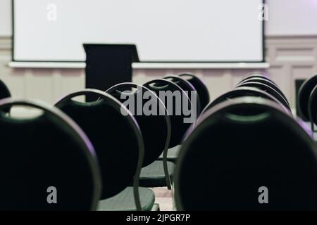 Ein abstraktes Bild einer leeren Reihe moderner Stühle in einem Konferenzraum des Hotels mit Blick auf eine weiße Platine Stockfoto