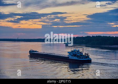 Bei Sonnenuntergang schwimmt ein Lastkahn auf dem Fluss. Sommerabendlandschaft. Stockfoto