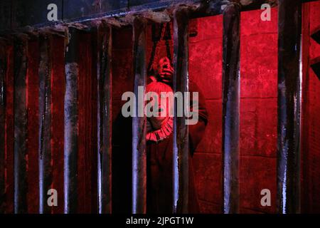 Eine Frau, die in einer Gefängniszelle mit buntem Lichteffekt angekettet wurde. Im Clink Prison Museum, Southbank Thames, London, Großbritannien. Stockfoto