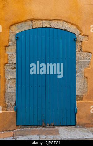 Alte blaue Holztür, umgeben von geschliffenen Steinen, auf einem Haus mit ockerfarbener Fassade in einer Straße in der Altstadt von Hyères, im Süden Frankreichs Stockfoto