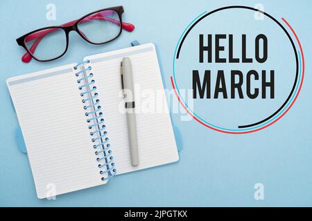 Eine Schrift mit dem Text „Hello March“ mit Notizblock und Brille auf blauem Hintergrund Stockfoto