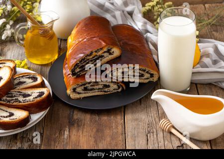 Rollen Sie mit Mohn und einem Glas Milch. Essen auf dem Tisch. Süßes, süßes Gebäck. Hausgemachtes einfaches Hefegebun mit Füllung. Frühstück auf einem Holztisch. Laktose und Gluten. Honigspas Stockfoto