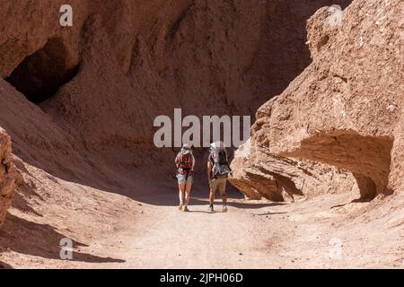 Ein paar Touristen wandern im Devil's Throat Canyon und tragen ihre beiden Kinder in Rucksäcken. Atacama-Wüste, Chile. Stockfoto