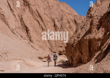 Ein paar Touristen wandern im Devil's Throat Canyon und tragen ihre beiden Kinder in Rucksäcken. Atacama-Wüste, Chile. Stockfoto