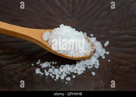 Teelöffel aus Holz voller Meersalz in einer dunklen Holzschüssel, weicher Fokus aus nächster Nähe Stockfoto