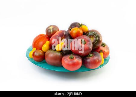 Verschiedene Tomatenfarben stapelten sich auf einem grünen Teller, isoliert auf weißem Hintergrund Stockfoto